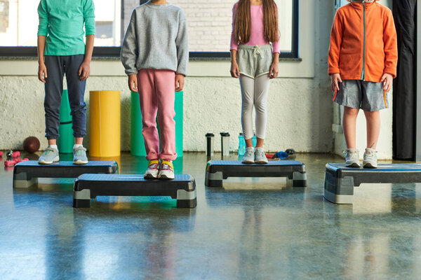 cropped view of four little children in sportswear standing on fitness steppers, child sport