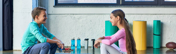 joyful boy and girl in sportswear sitting and smiling cheerfully at each other, child sport, banner