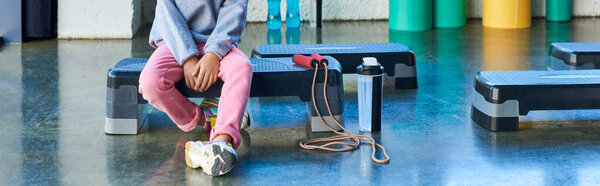 cropped view of little girl sitting on fitness stepper with water bottle, child sport, banner