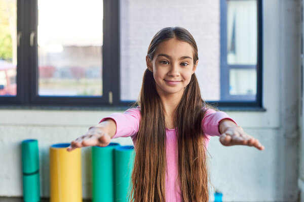 pretty preadolescent girl smiling at camera and stretching her arms in front of her, child sport