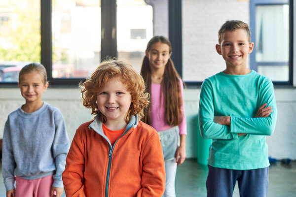 four cheerful preadolescent children posing in gym and smiling joyfully at camera, child sport