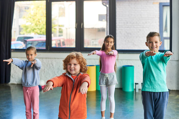 jolly boys and girls in sportswear stretching with hands in front of them, smiling at camera, sport