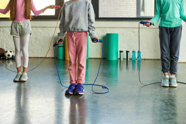 cropped view of three preadolescent children in sportswear holding jump ropes, child sport