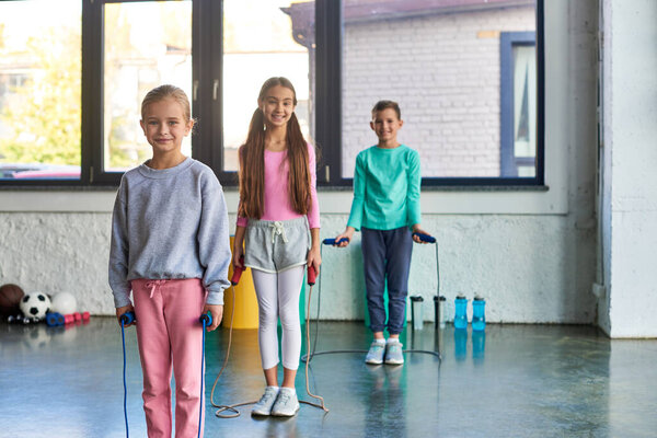 cheerful little cute boy and girls smiling joyfully at camera and holding jump ropes, child sport