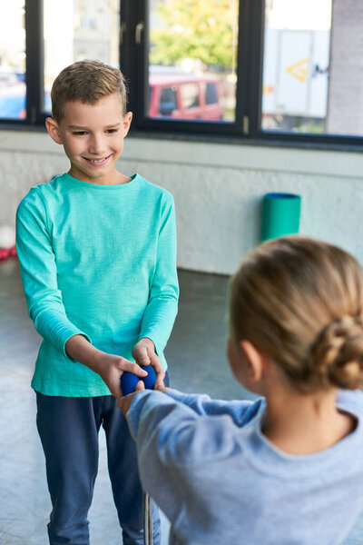 vertical shot of preadolescent cute boy and girl holding jump rope and smiling at each other, sport
