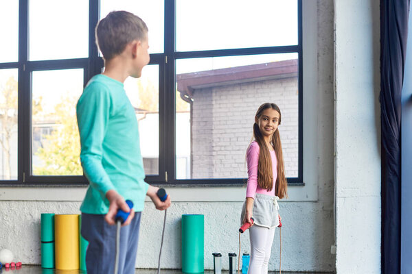 pretty preadolescent children with skipping ropes in hands smiling at each other, child sport