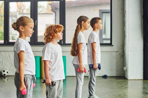 preadolescent boys and girls posing in profile in gym with dumbbells in their hands, child sport