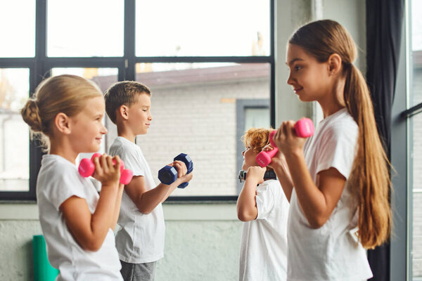 focus on preadolescent boys with dumbbells posing near blurred cute girls, workout, child sport