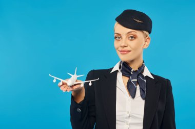 Üniformalı zarif bir hostes uçak modelini tutuyor ve kamera karşısında gülümsüyor.
