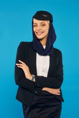 Arap havayollarının çekici hostesi üniformalı, başörtüsü takmış mavi kollarıyla poz veriyor.