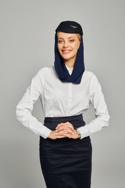 Arap havayollarının başörtüsü ve beyaz bluzuyla gri kameraya gülümseyen hostesi.