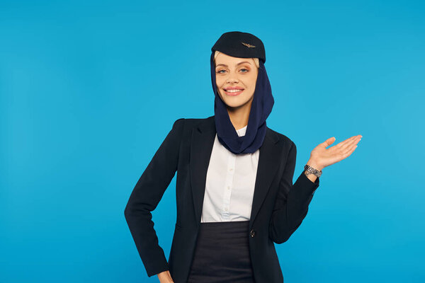arabian airlines hospitality, smiling stewardess in headscarf and uniform showing direction on blue