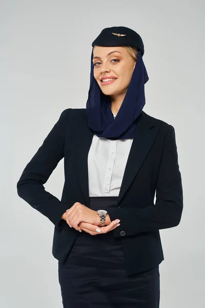 stock image graceful stewardess of arabian airlines with happy smile and headscarf looking at camera on grey