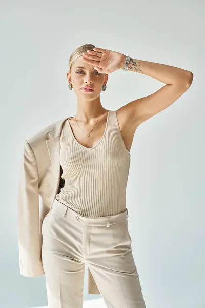 stock image glamour woman posing with hand near forehead and blazer on shoulder on grey, beauty and style