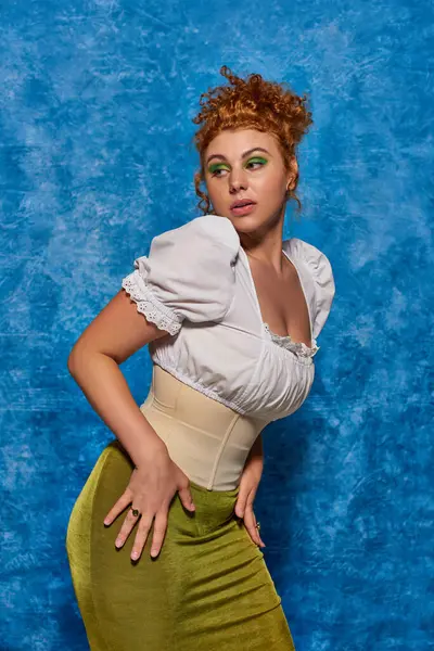 stock image seductive redhead plus size model in white stylish blouse looking away on blue textured backdrop