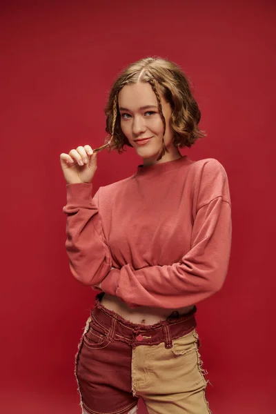 stock image personal style, pretty gen z woman in patchwork pants and cropped long sleeve gesturing on red