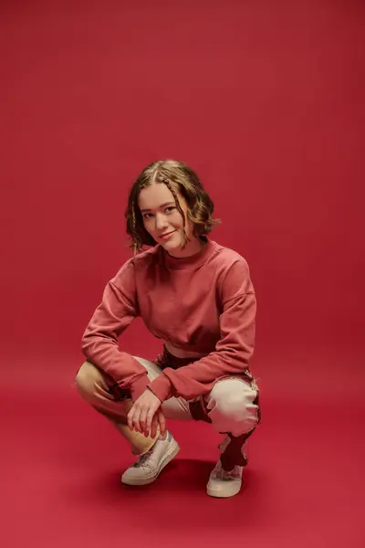 personal style, young woman in patchwork pants and cropped long sleeve sitting on red backdrop
