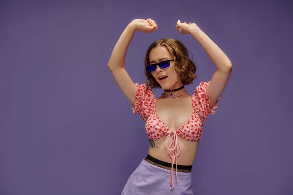 self-expression, young woman in cropped top with hearts and sunglasses singing with raised hands