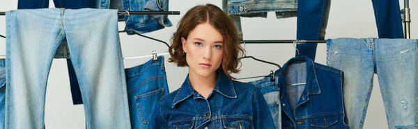 chic young model in denim jacket and jeans posing among jeans  clothes on grey backdrop, banner
