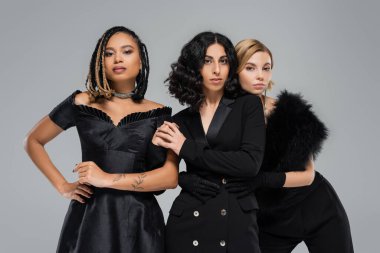 Tamamen siyah giyinmiş zarif çok ırklı kız arkadaşlar gri, kendinden emin bir şekilde kameraya bakıyorlar.