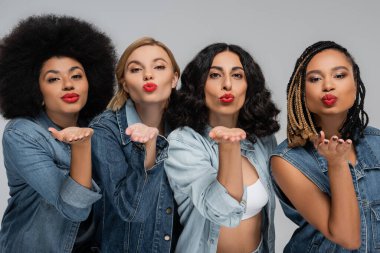 Çok ırklı kız arkadaşları cezbediyor mavi kot kıyafetler kameraya hava öpücüğü veriyor, modern moda.