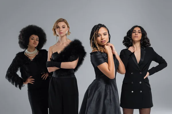 stock image diverse multiracial girlfriends in black stylish attire looking at camera on grey, high fashion