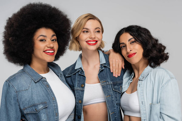positive multicultural diverse models in blue denim outfits smiling on grey, friendship and fashion