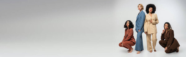 fashion banner, diverse group of multiethnic barefoot girlfriends in colorful suits on grey backdrop