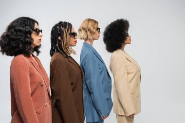 Koyu güneş gözlüklü ve gri takım elbiseli çok kültürlü kız arkadaşların yan görünüşü