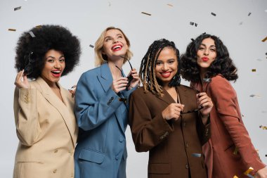 Renkli konfeti altında güneş gözlüğü takan şık takım elbiseli çok ırklı kızlar, parti