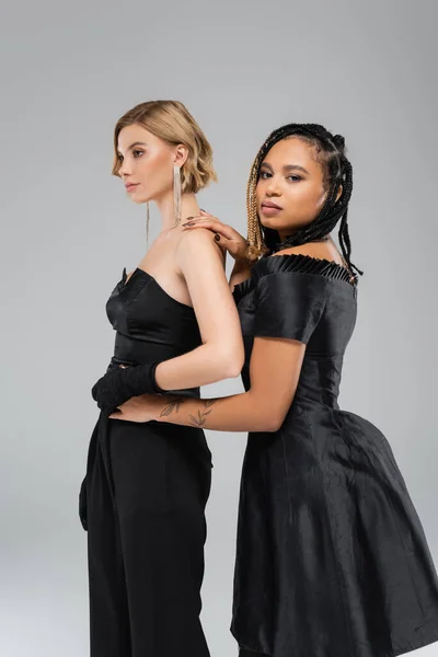 stock image elegant african american woman in black attire embracing waist of blonde glamour friend on grey