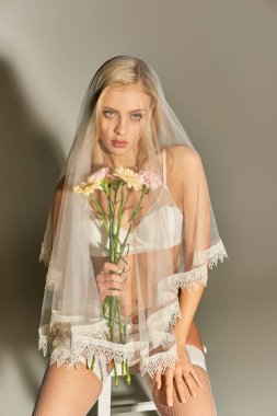 vertical shot of sexy young woman in erotic lingerie with veil holding flowers sitting on tall chair clipart