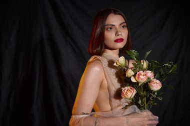 Romantik şeffaf elbiseli çekici genç bir kadın elinde çiçek açan güller tutuyor.