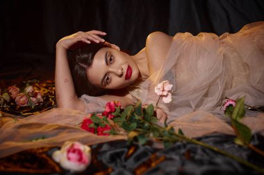 Güzel ve şehvetli, şeffaf elbiseli genç bir kadın çiçek açan çiçeklerin arasında yatıyor.