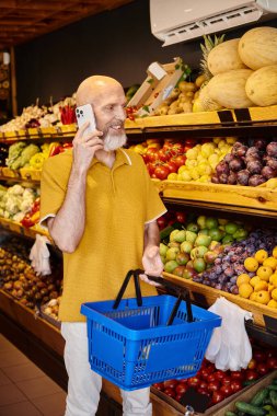 Alışveriş sepeti olan olgun bir erkek müşteri market alışverişini yaparken telefonla konuşuyor.