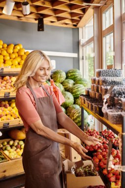 Neşeli çekici satıcı markette gülümsüyor ve elinde bir paket taze çilek tutuyor.
