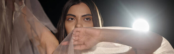 sensual young woman with brunette short hair posing in transparent dress on black backdrop, banner