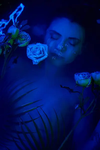 feminine beauty, young woman diving underwater among palm leaves and flowers, blue light