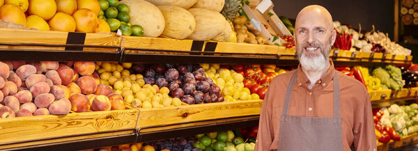 jolly mature bearded seller smiling happily at camera posing with stall on backdrop, banner