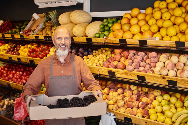 cheerful gray bearded seller posing with fresh delicious blackberries in hands and smiling joyfully