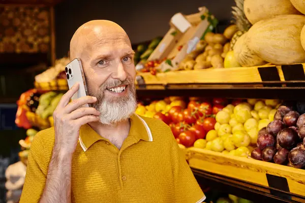 gray bearded mature customer talking by phone at grocery store and smiling joyfully at camera