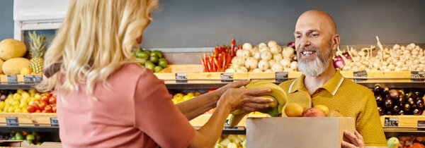 focus on smiling man looking at blurred female seller putting fresh bananas into paper bag, banner