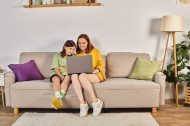 Genç kızı olan mutlu bir kadın dizüstü bilgisayarda film izliyor oturma odasında, kaliteli zaman geçiriyor.