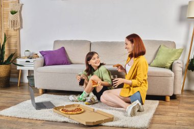 Pizza ve gazozlu mutlu anne ve kız oturma odasında dizüstü bilgisayarda film izliyorlar.
