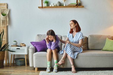 Endişeli bir anne evde başı eğik oturan depresif bir genç kızı sakinleştiriyor.
