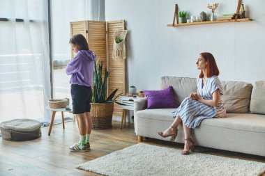 offended teen girl standing with folded arms near displeased mother on couch, family conflict clipart