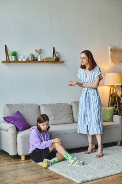serious woman talking to frustrated teenage daughter sitting on floor in living room, generation gap clipart