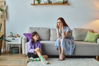 frustrated woman touching head near teenage daughter sitting on floor in living room, conflict clipart