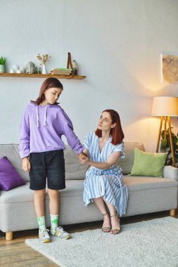 Endişeli ve üzgün bir kadın hayal kırıklığına uğramış genç kızın elini tutuyor oturma odasında, kuşak farkı