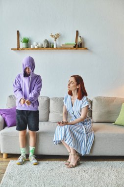 worried and upset woman talking to offended daughter hiding in hood in living room, generation gap clipart